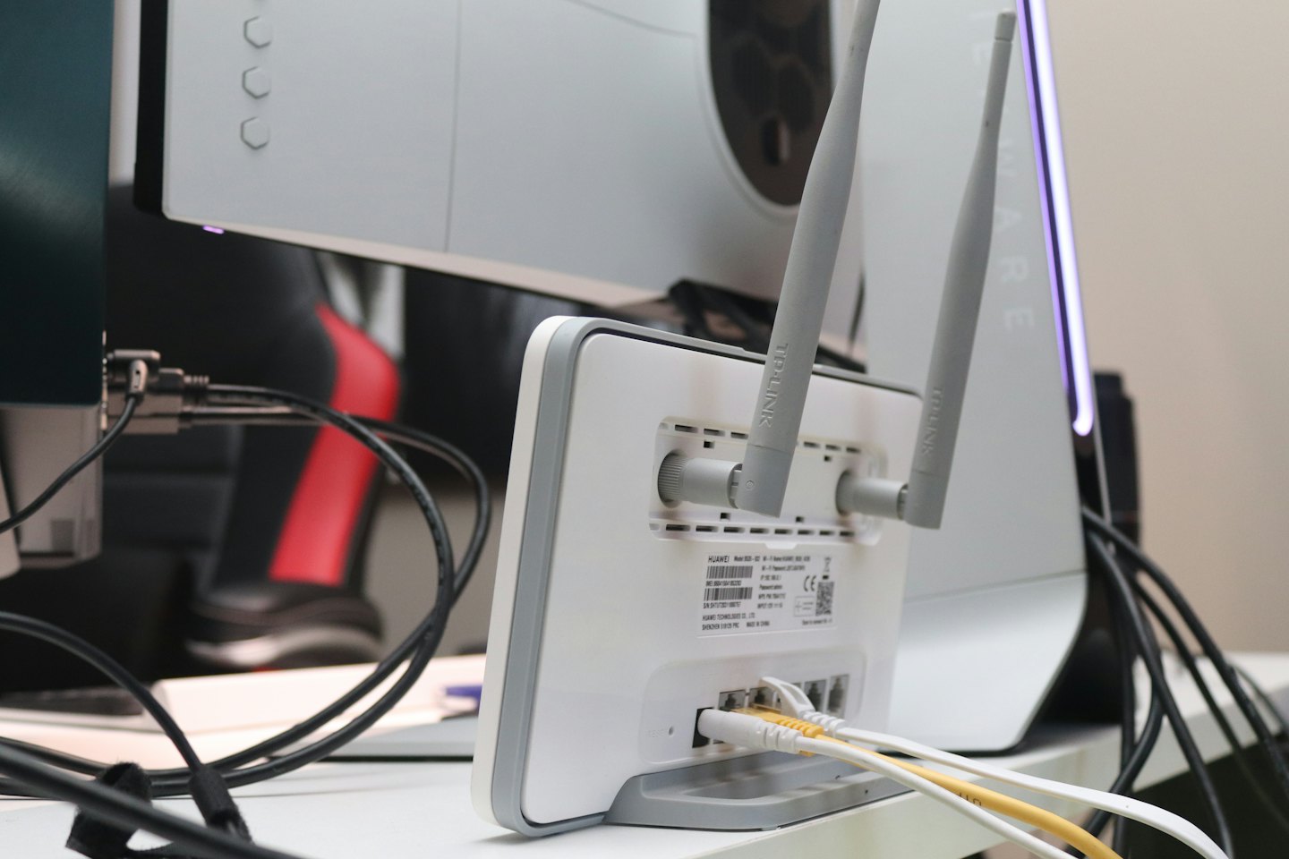Weißer und grauer Router mit Antennen und Ethernet-Kabeln auf einem Schreibtisch.